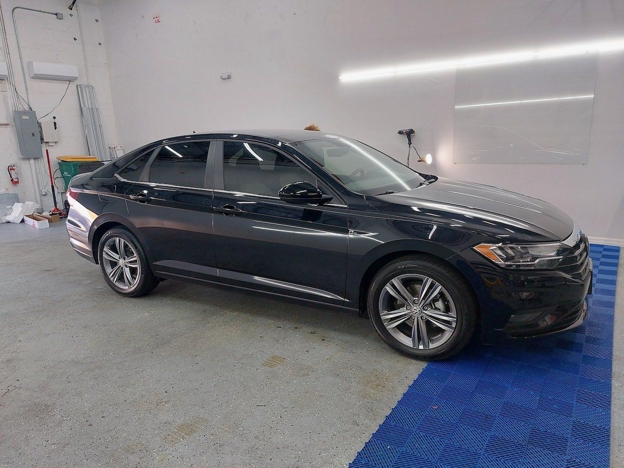 A black car is parked in a garage next to a blue mat.