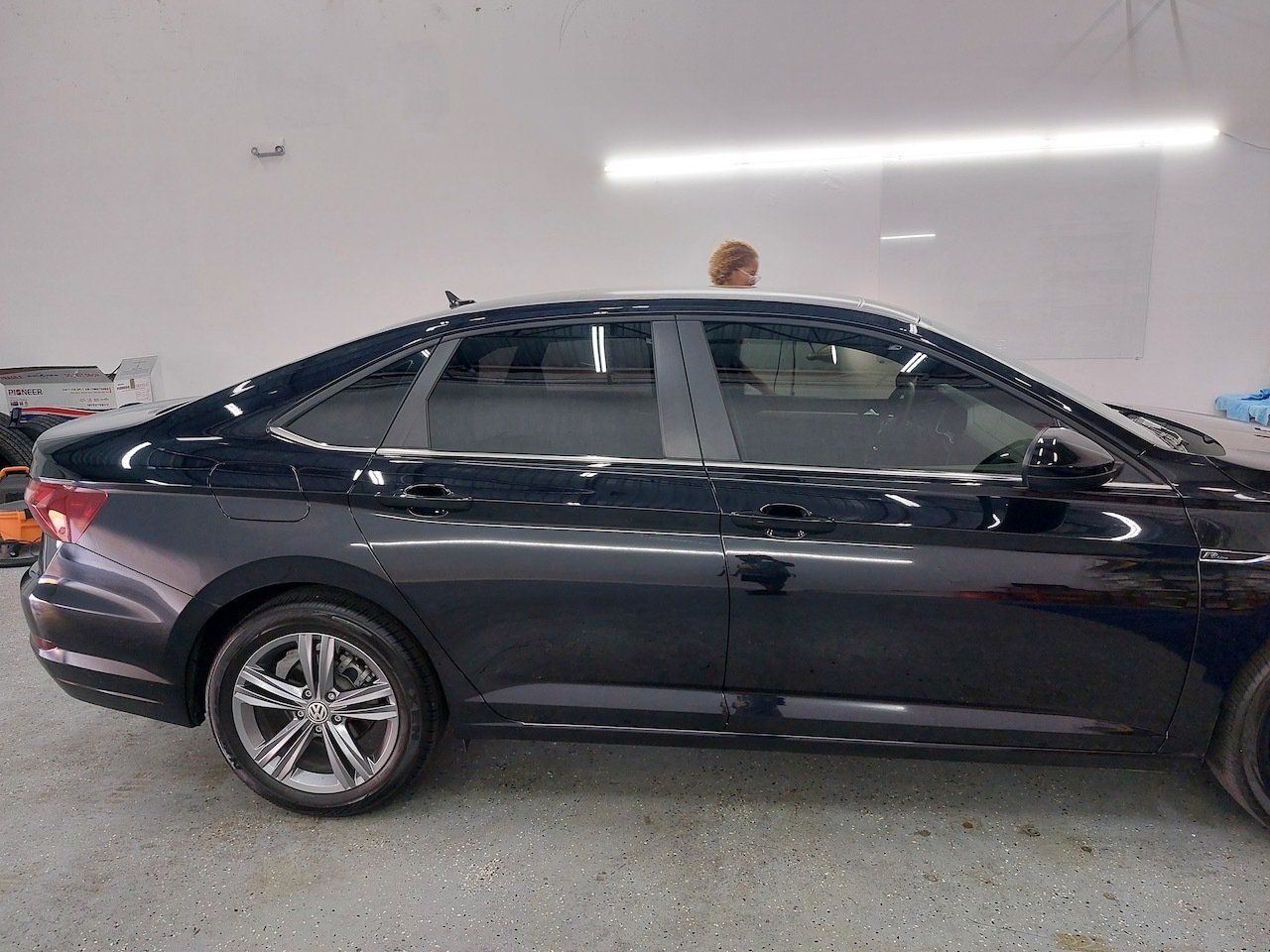 A black car is parked in a garage next to a white wall.