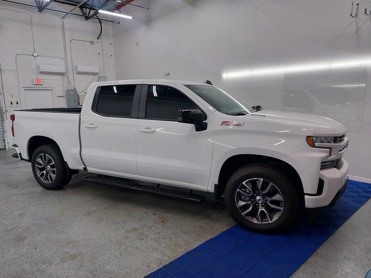 A white truck is parked in a garage on a blue mat.