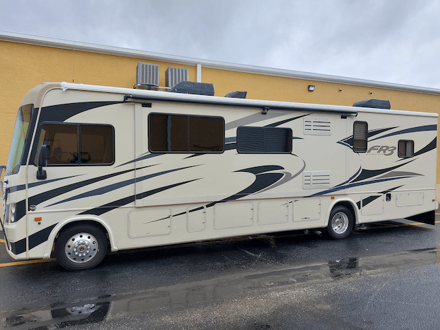 A large white rv is parked in front of a yellow building