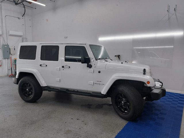 A white jeep wrangler is parked in a garage.