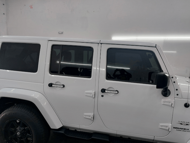 A white jeep is parked in front of a white wall.