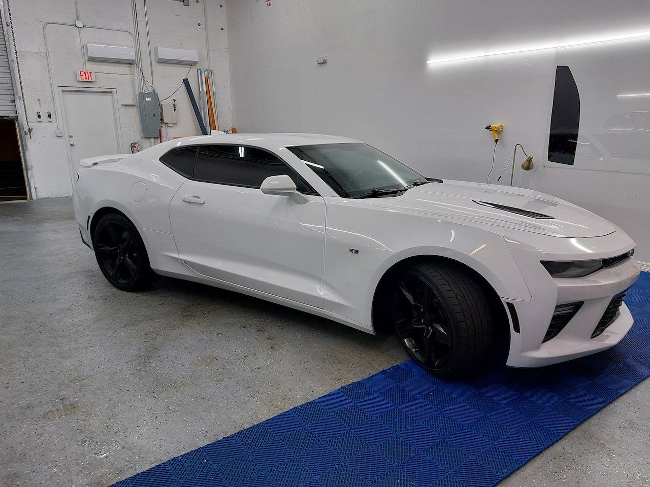 A white car is parked on a blue mat in a garage.