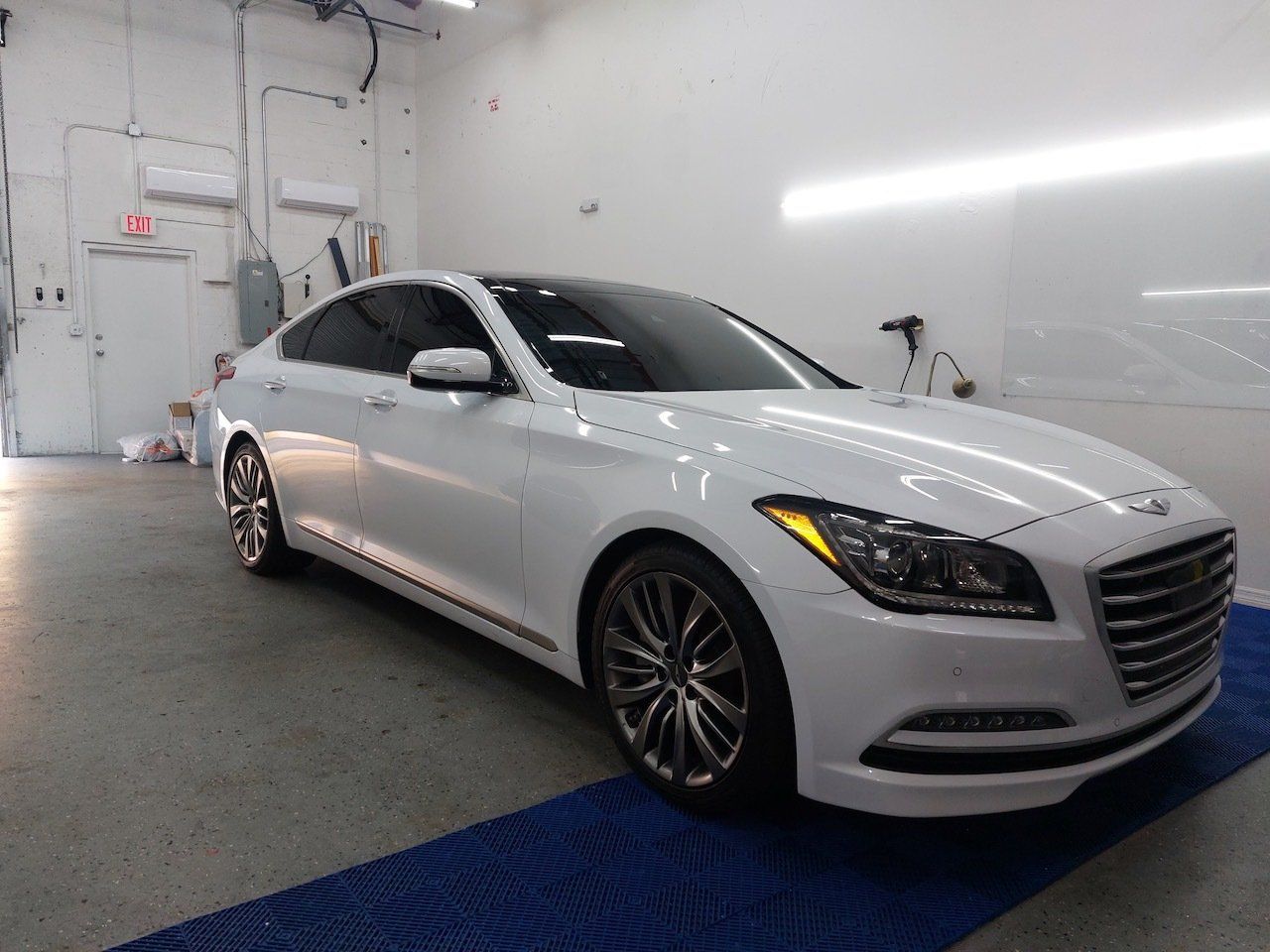 A white hyundai genesis is parked in a garage.