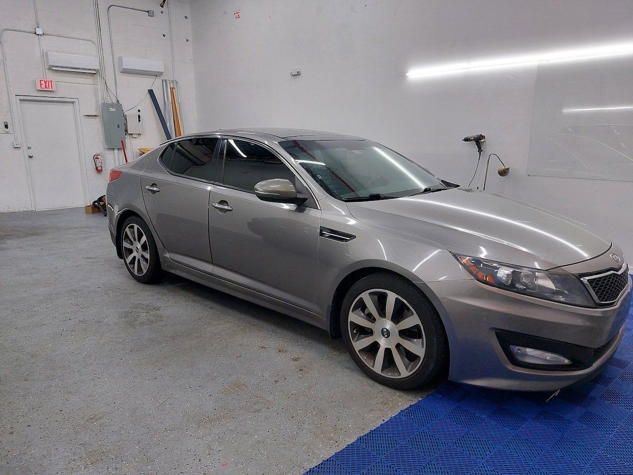 A silver car is parked in a garage next to a blue mat.
