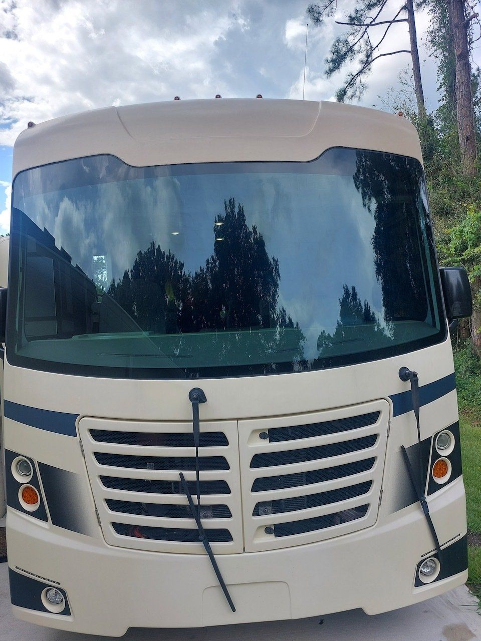 A white rv is parked in a driveway with trees in the background