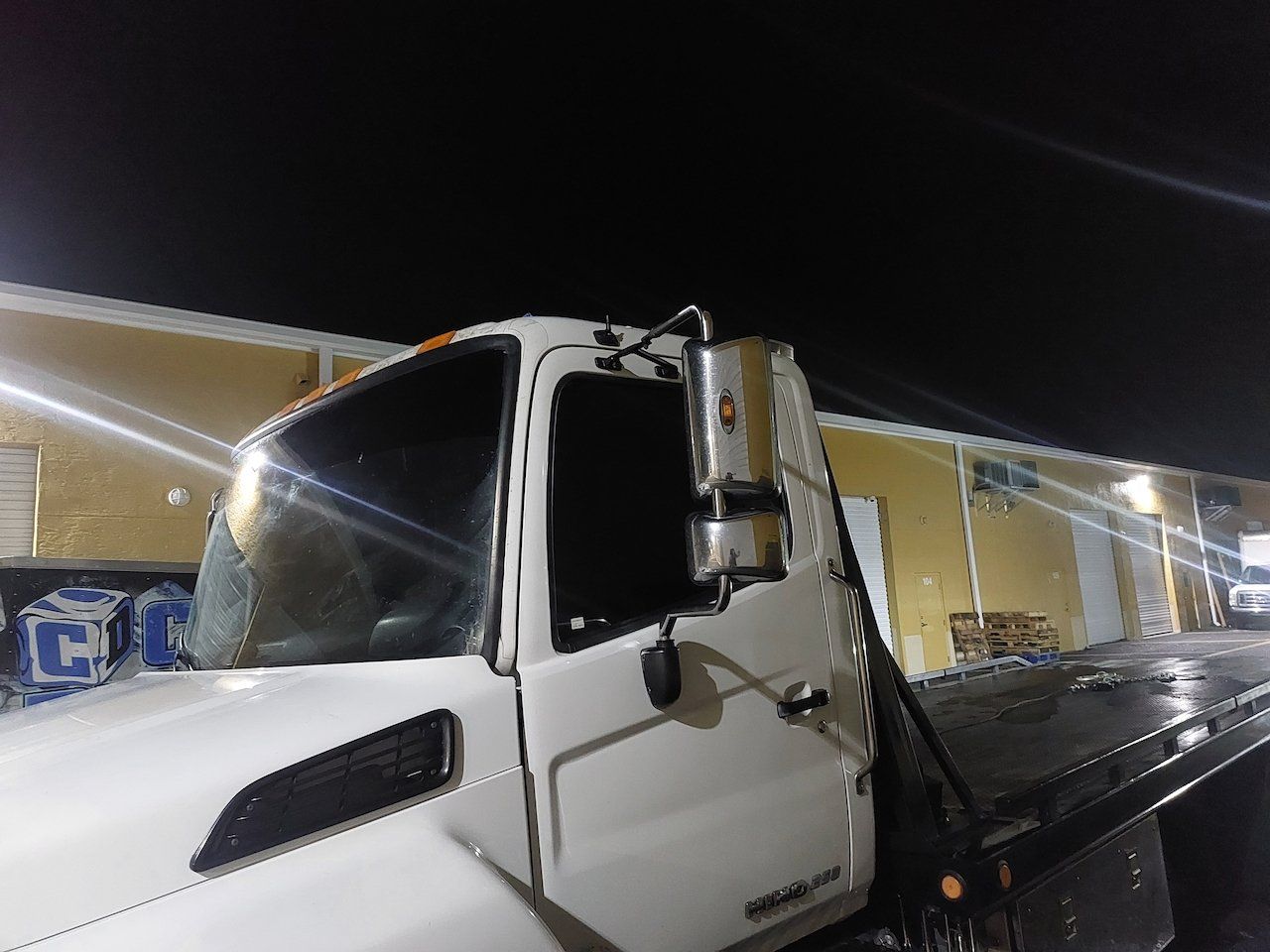 A white tow truck is parked in front of a building at night.