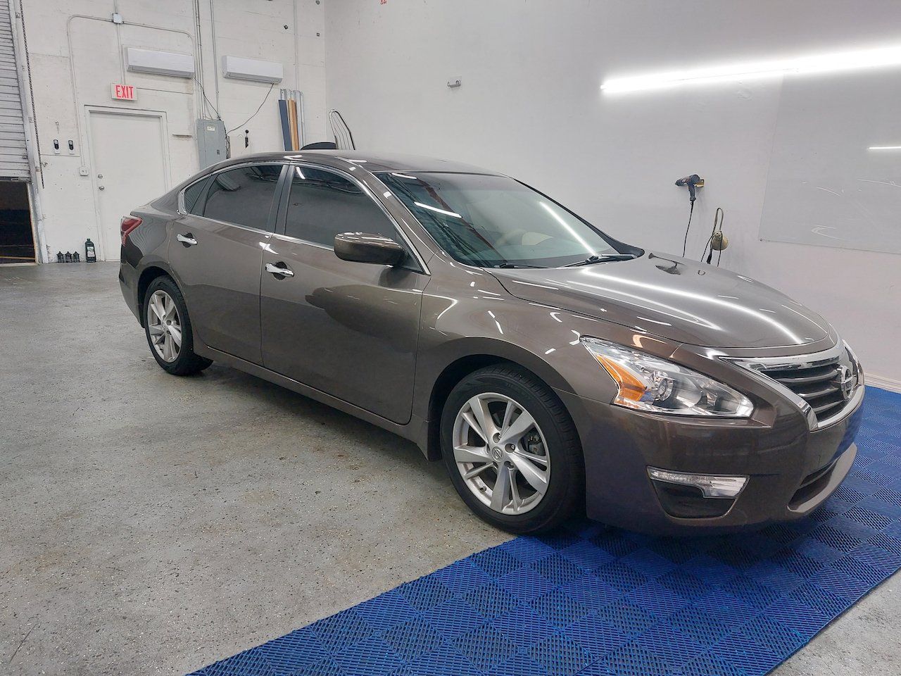 A brown nissan altima is parked on a blue mat in a garage.