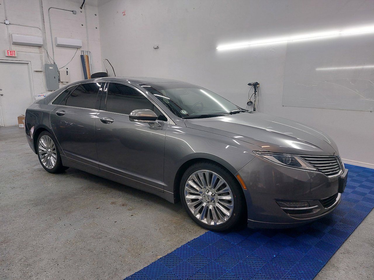 A gray car is parked on a blue mat in a garage.
