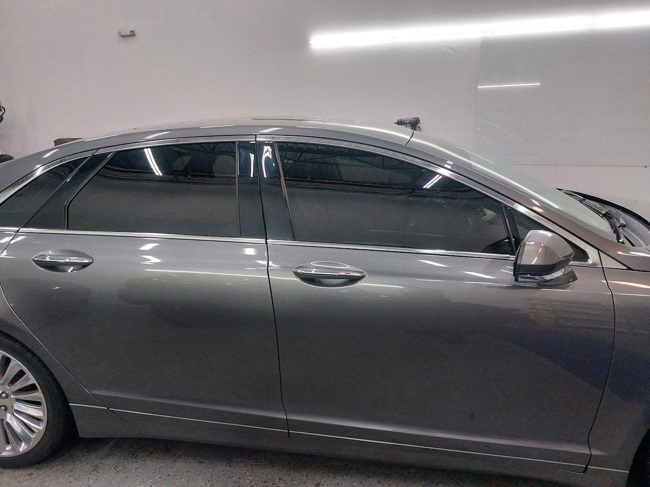 A silver car is parked in a garage next to a white wall.