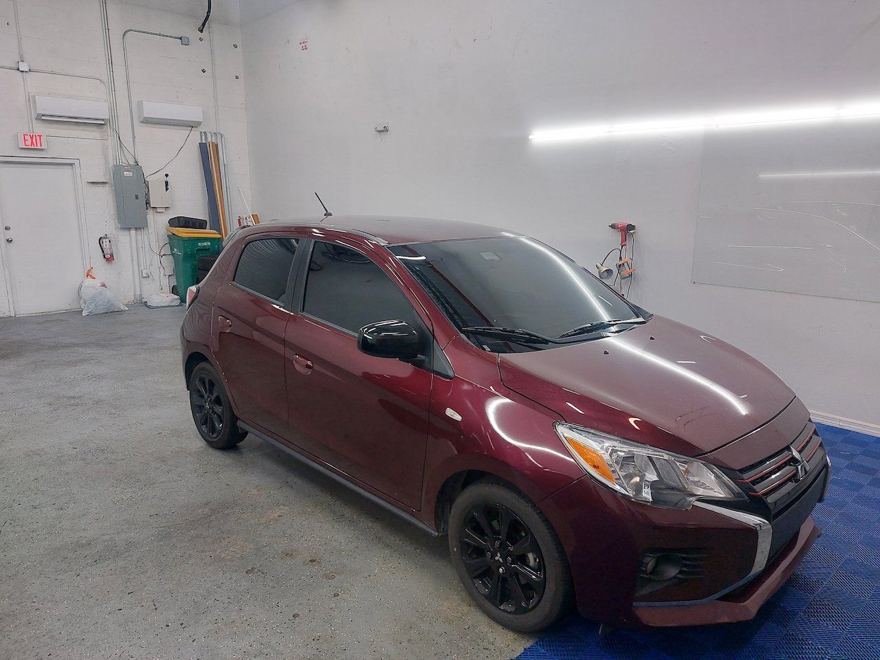 A red car is parked in a garage on a tarp.