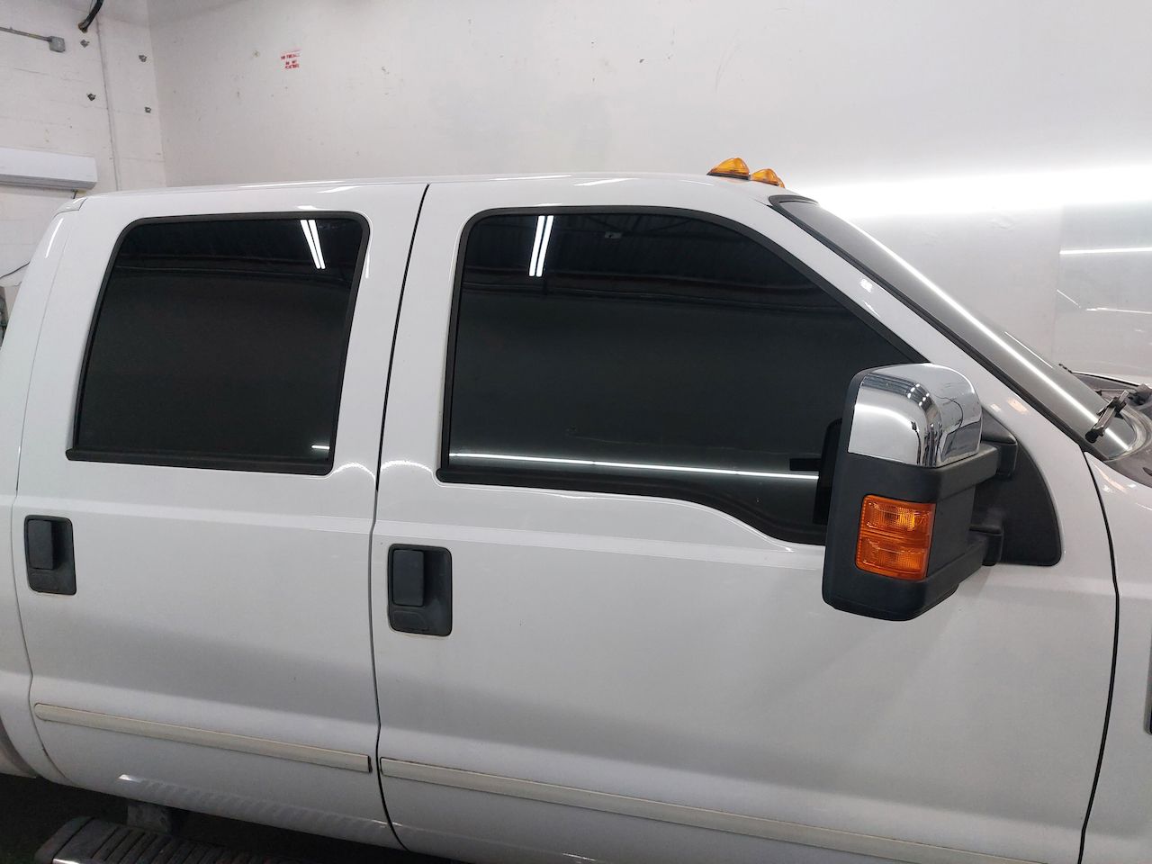 A white truck with black windows is parked in a garage.