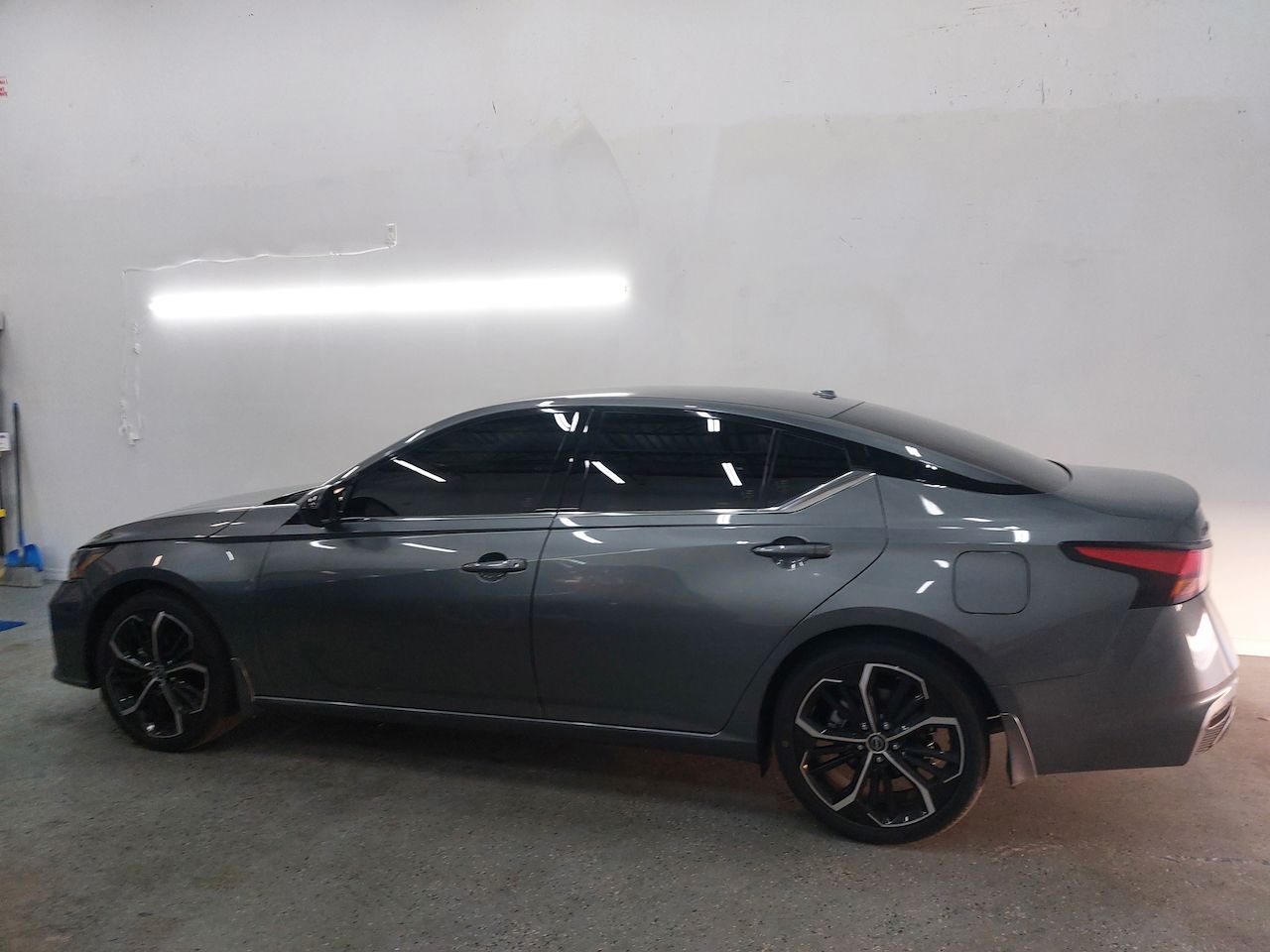 A gray car is parked in a garage next to a white wall.