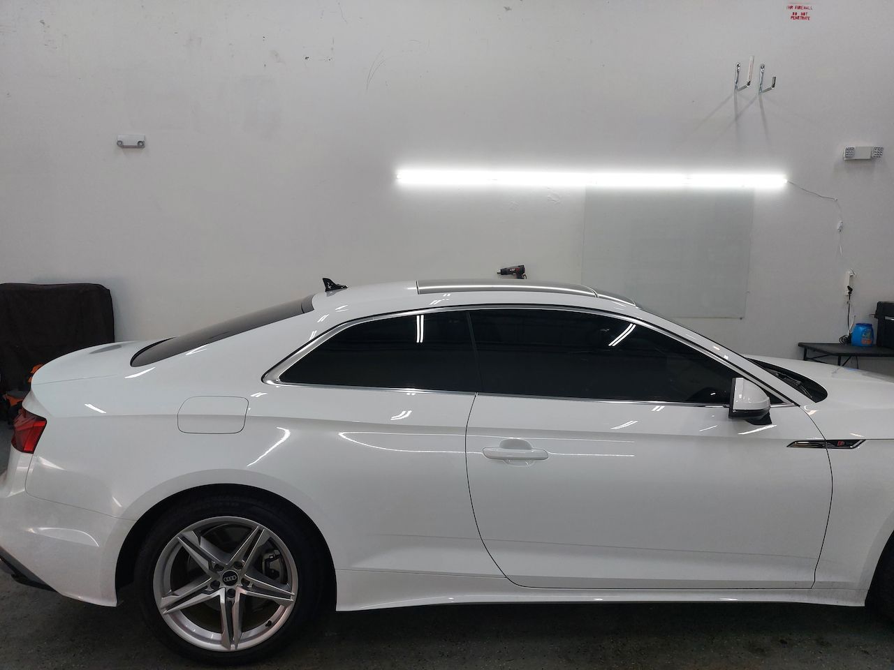 A white car is parked in a garage under a light.