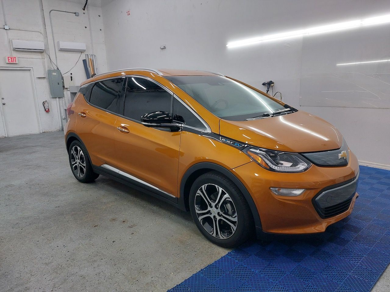 An orange chevrolet bolt electric car is parked in a garage.