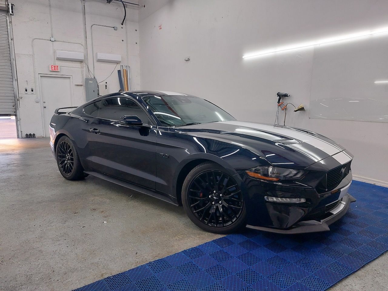 A black ford mustang is parked in a garage on a blue mat.