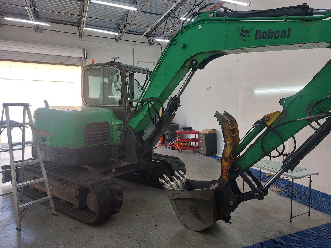 A green bobcat excavator is parked in a garage.