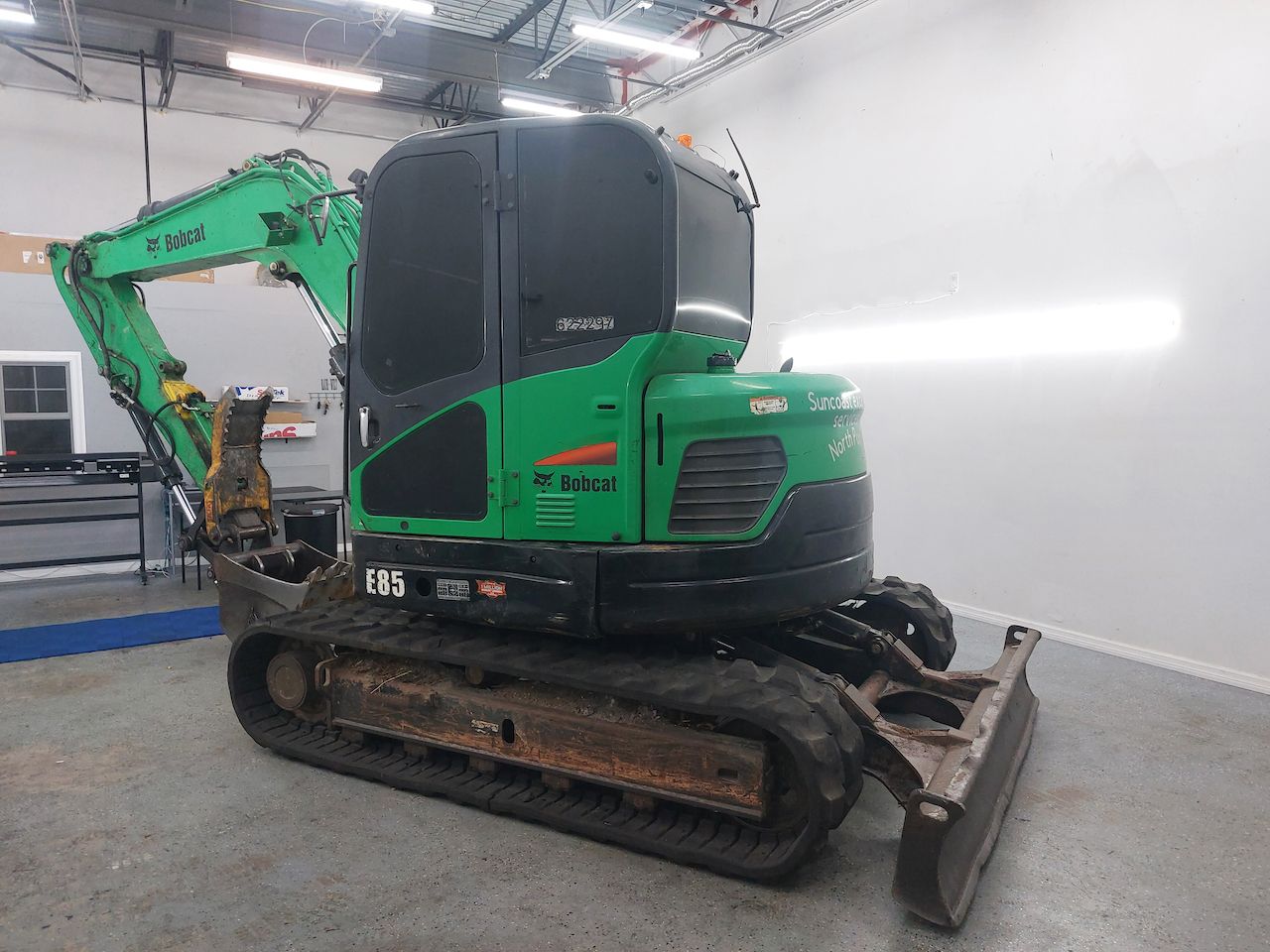 A green and black excavator is parked in a garage.
