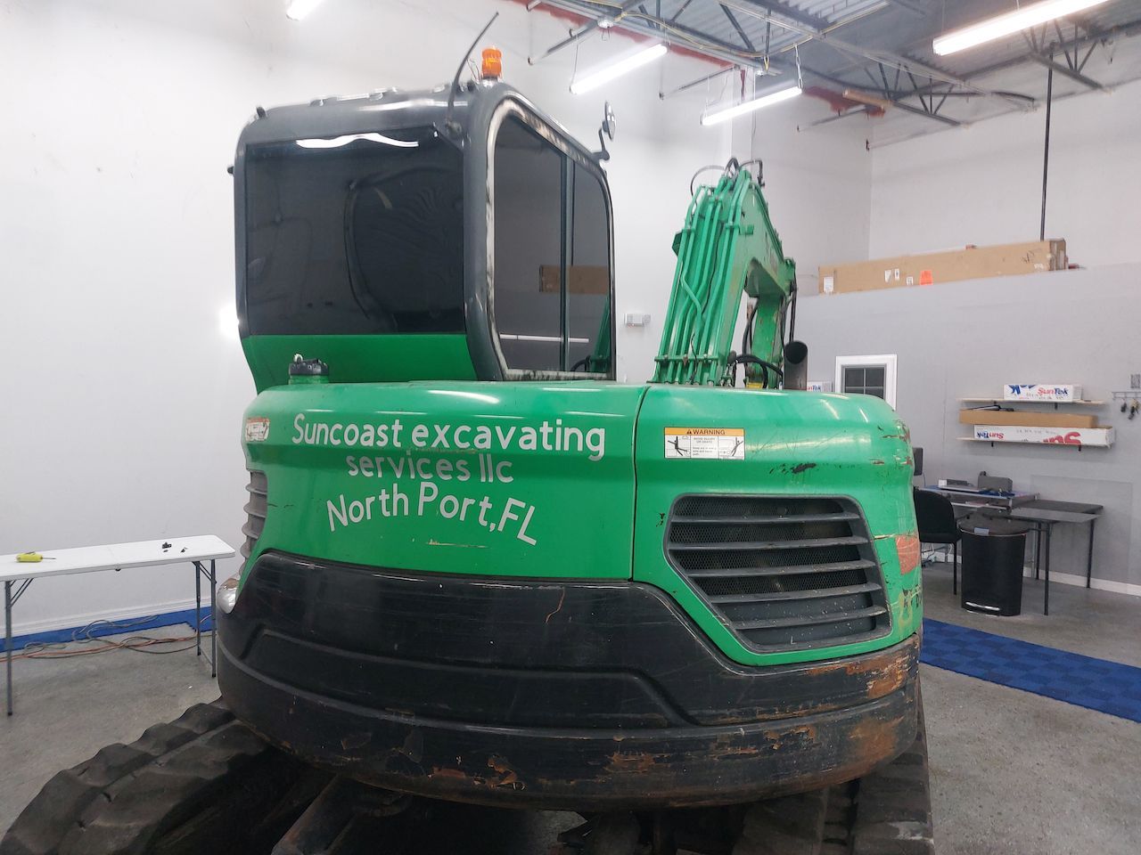 A green excavator is parked in a garage with the words suncoast excavating services written on it