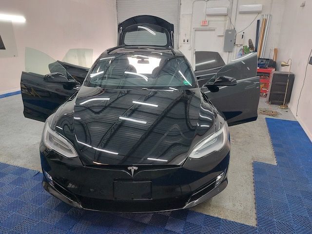 A black tesla model s is parked in a garage with its doors open.