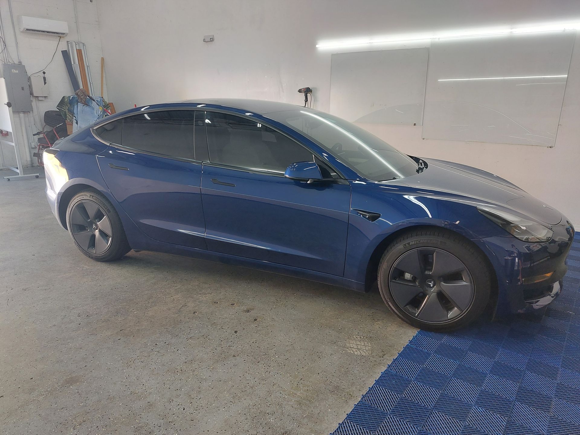 A blue tesla model 3 is parked in a garage.