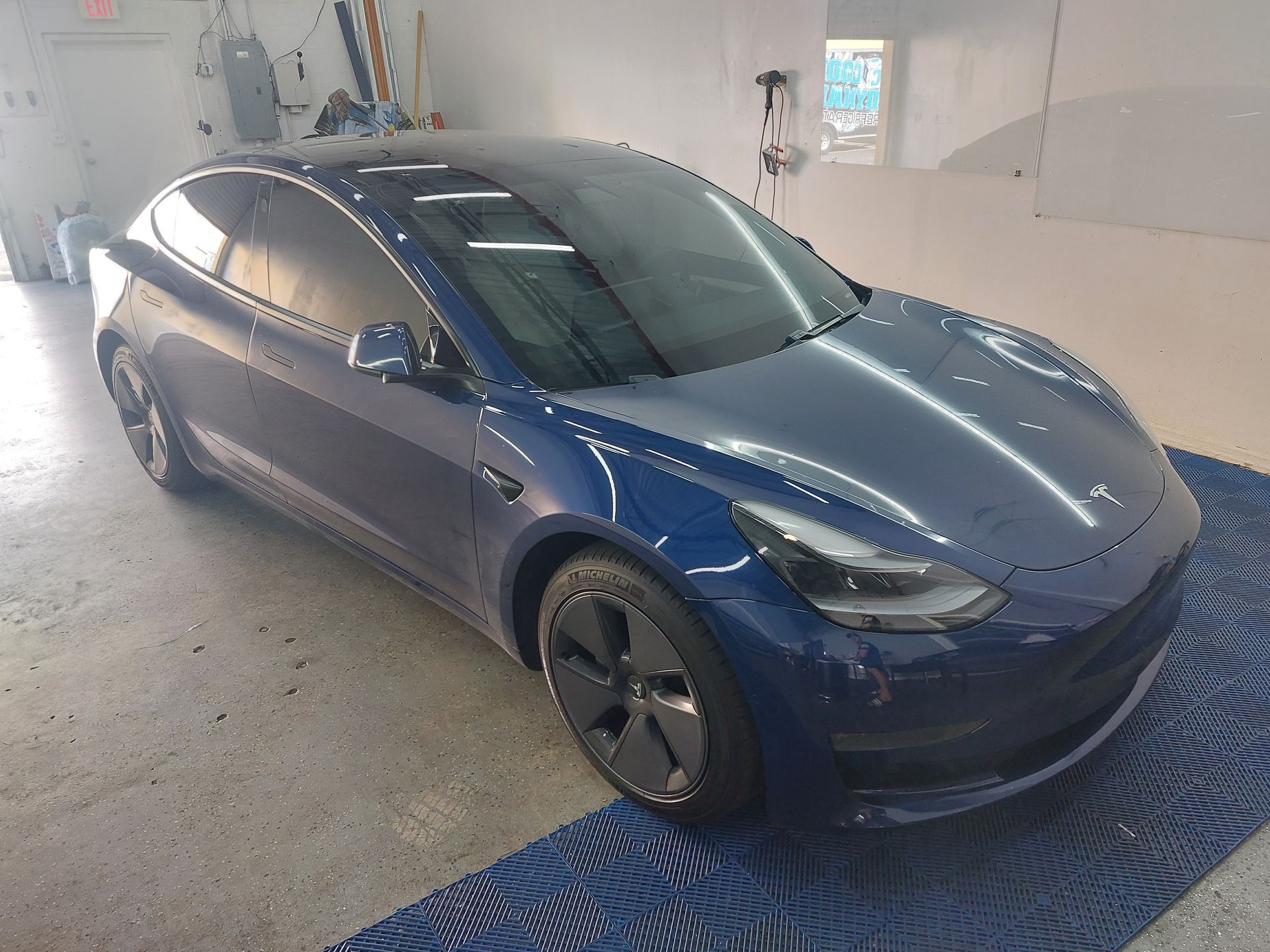 A blue tesla model 3 is parked in a garage.