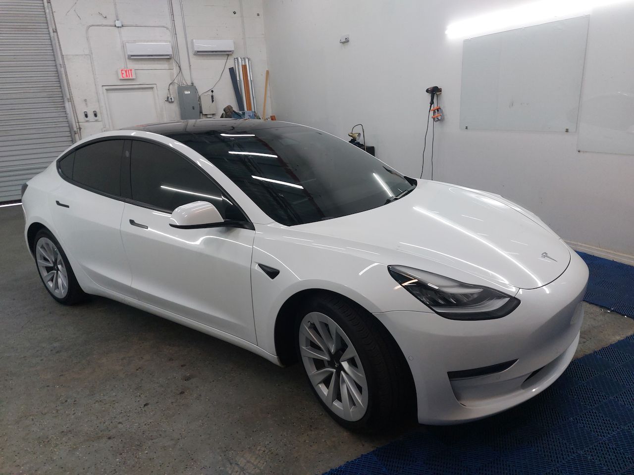 A white tesla model 3 is parked in a garage.