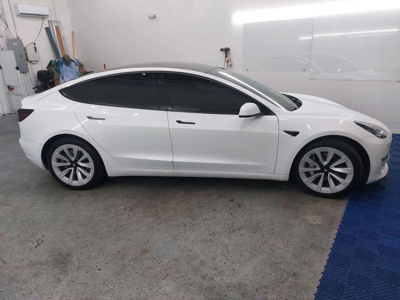 A white tesla model 3 is parked in a garage.