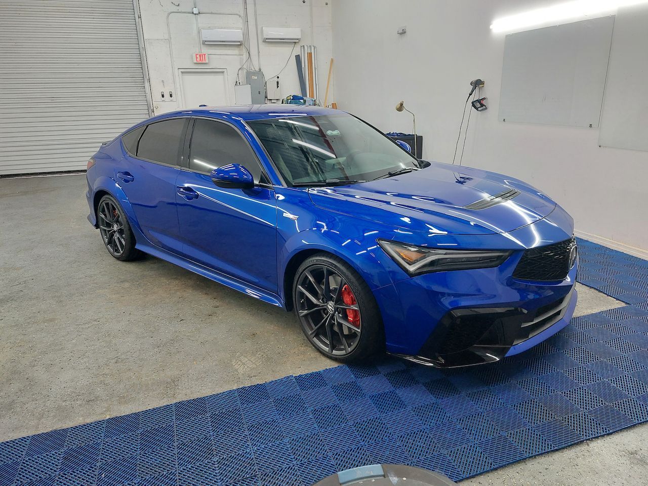 A blue car is parked in a garage on a blue mat.