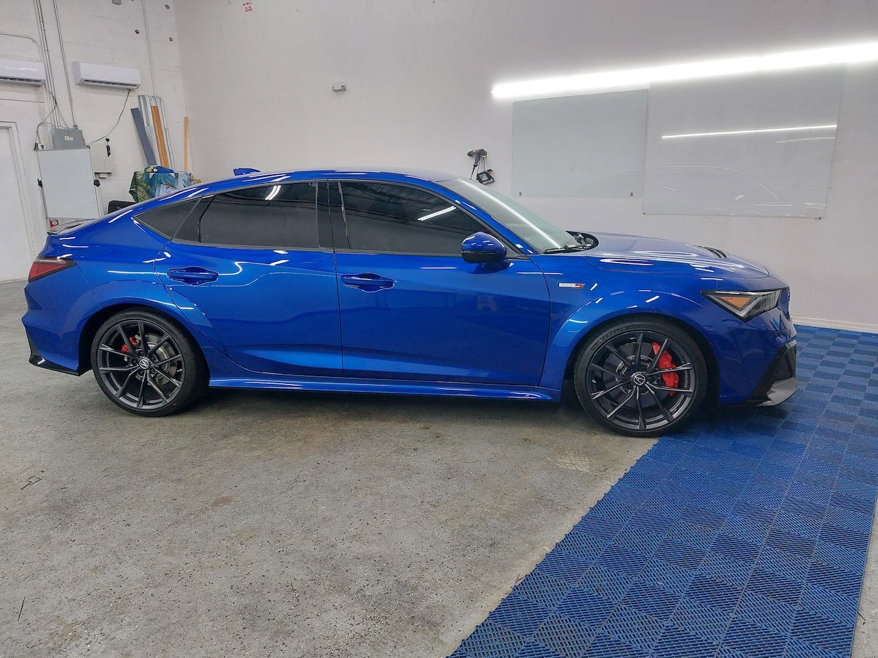 A blue car is parked in a garage next to a blue mat.