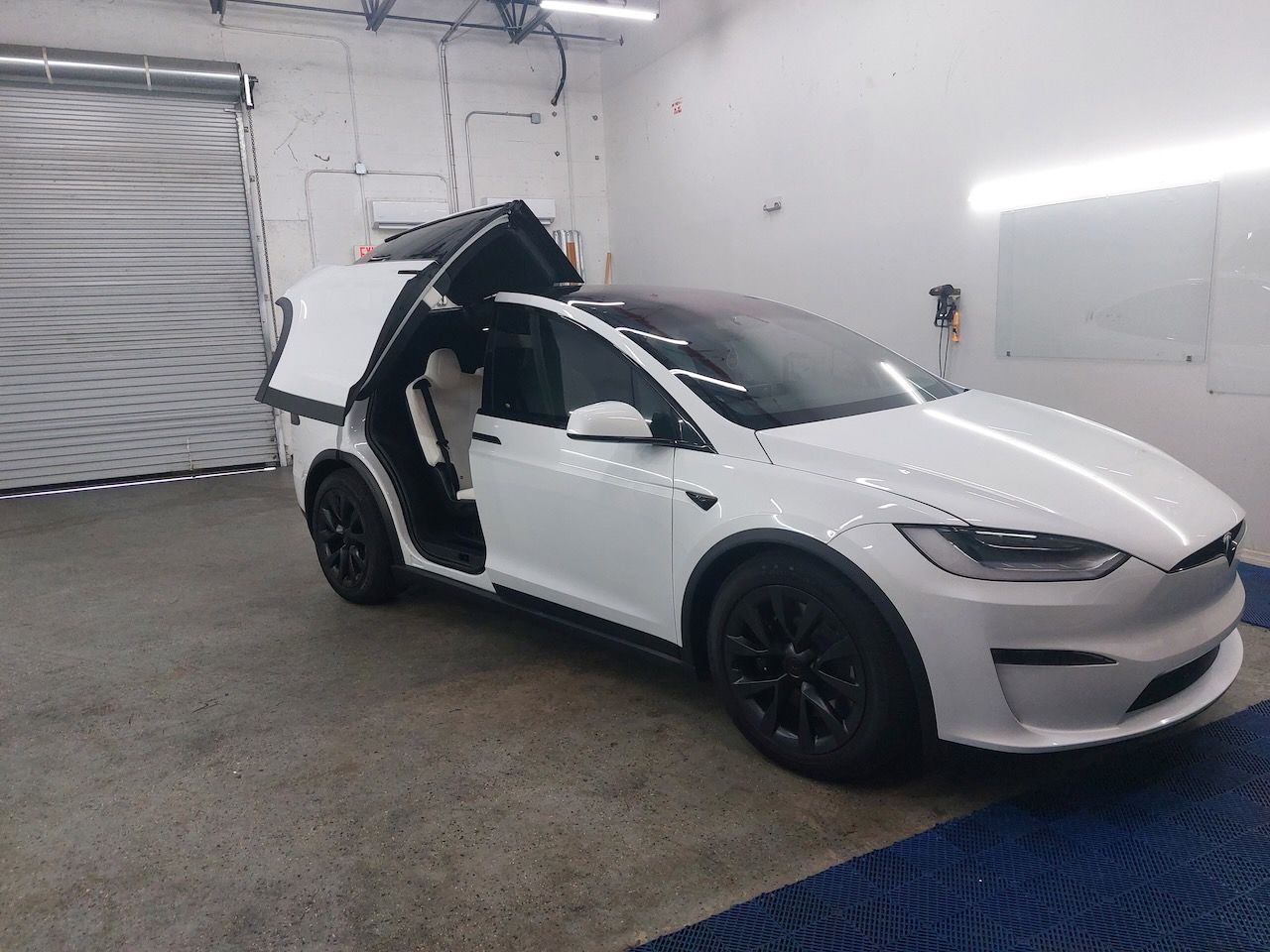 A white tesla model x is parked in a garage with its doors open.