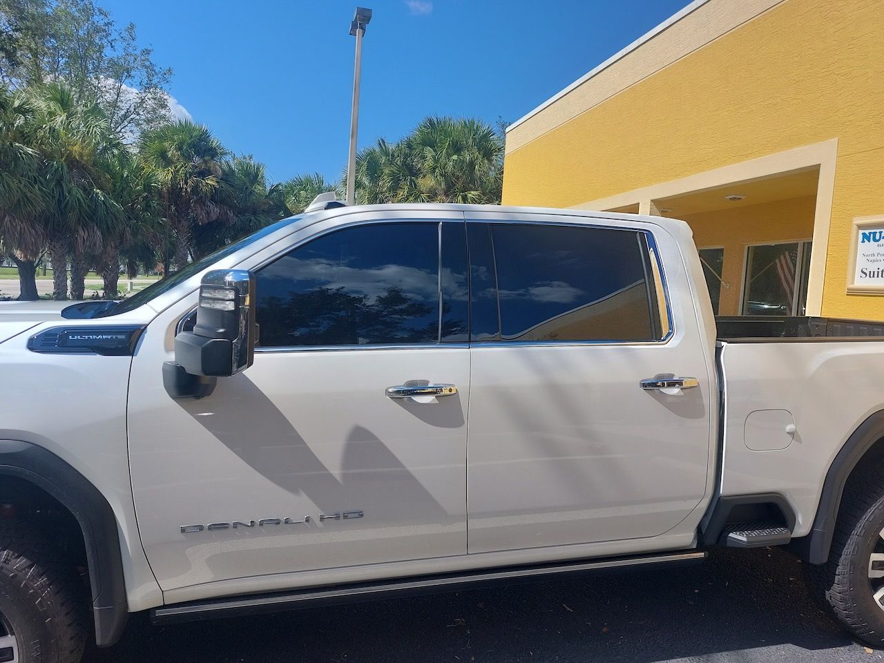 A white truck is parked in front of a yellow building.