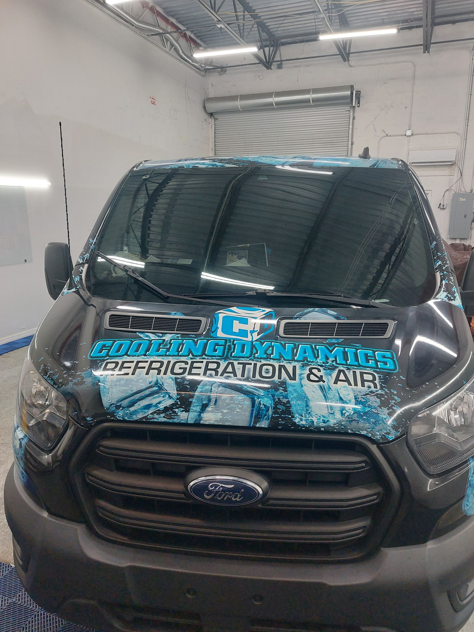 A ford van with a wrap on the front is parked in a garage.