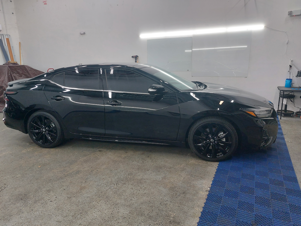 A black car is parked in a garage next to a blue mat.