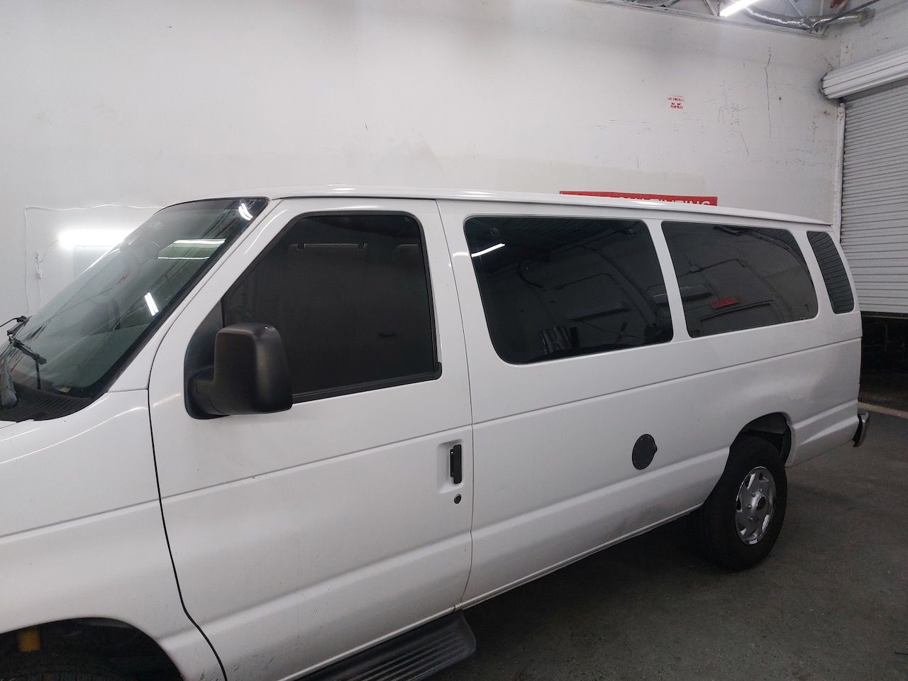 A white van with black windows is parked in a garage.