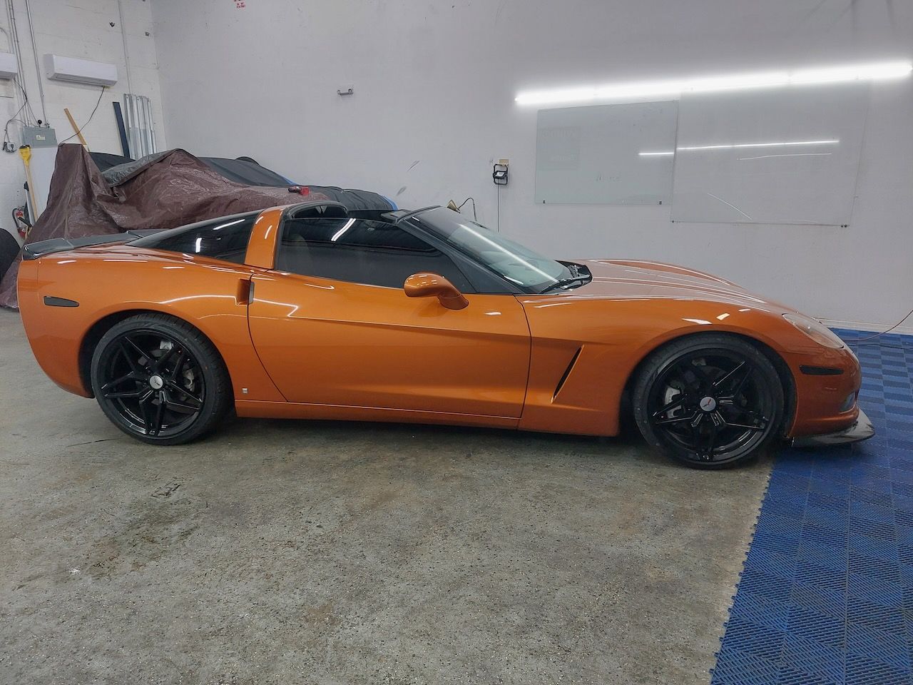 An orange corvette is parked in a garage.