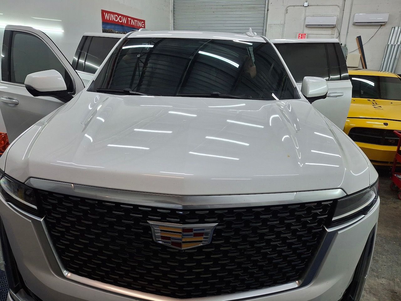 A white cadillac is parked in a garage next to a yellow car.