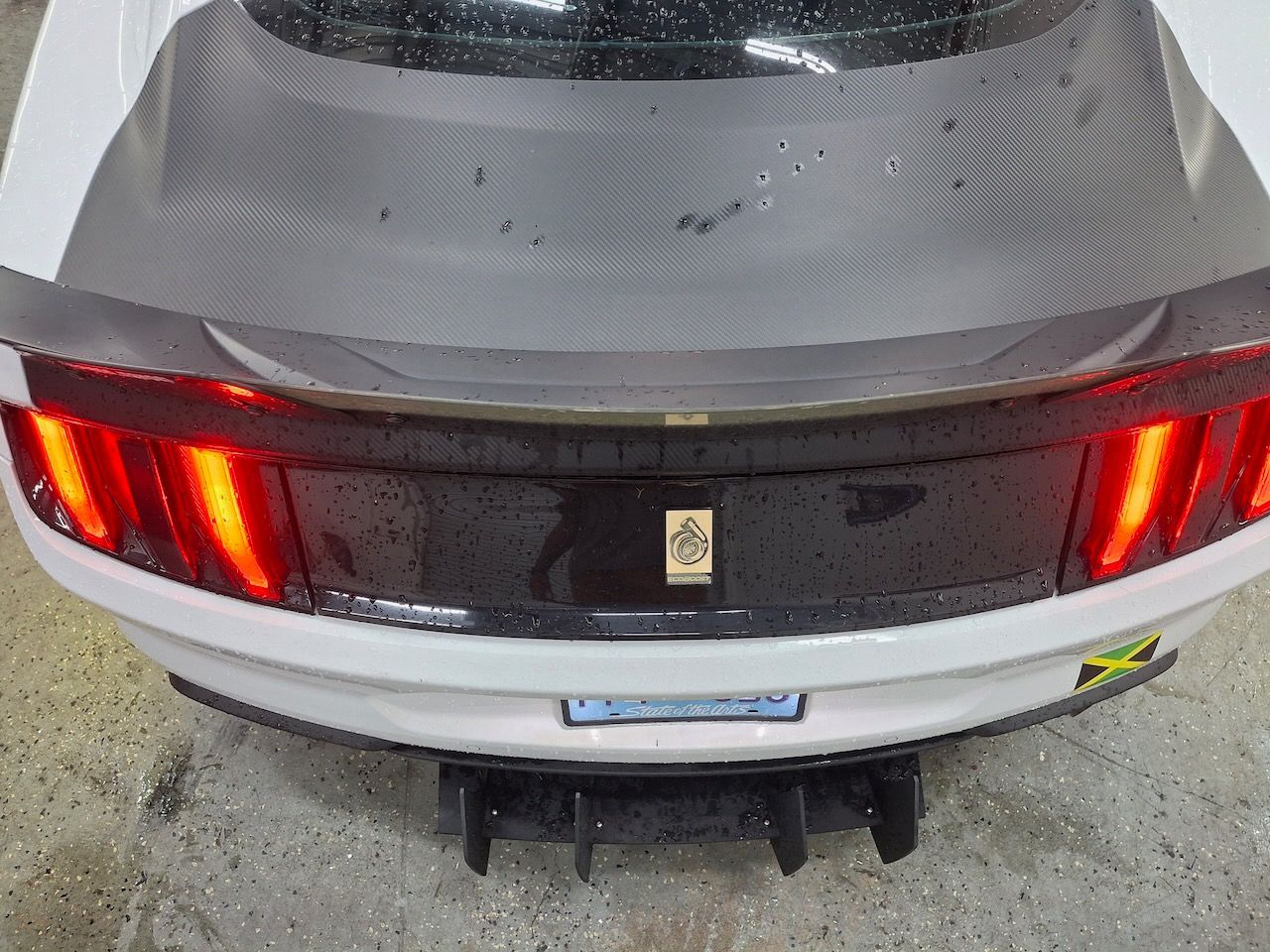 The rear end of a white car with a carbon fiber spoiler.