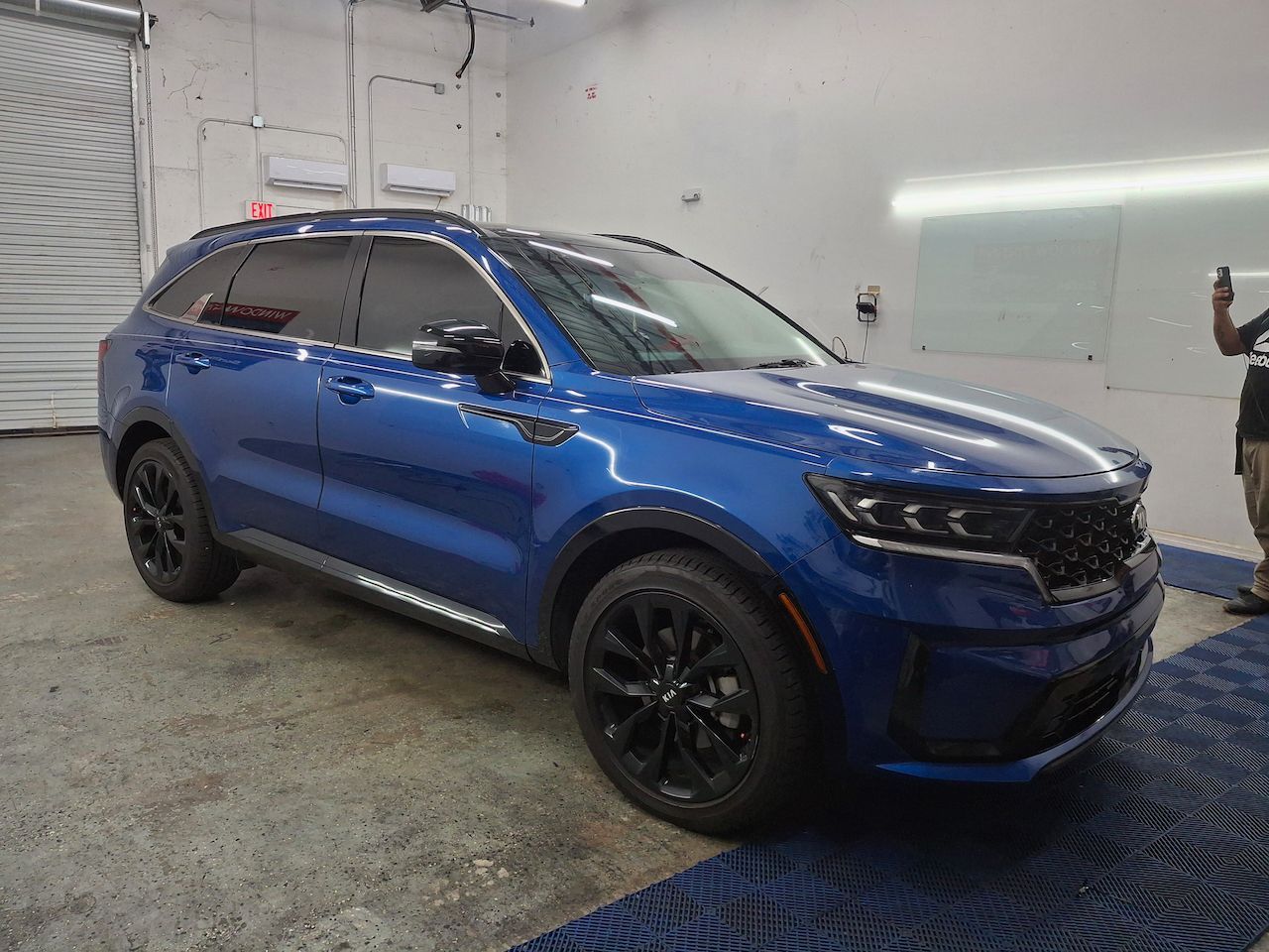A man is standing next to a blue suv in a garage.