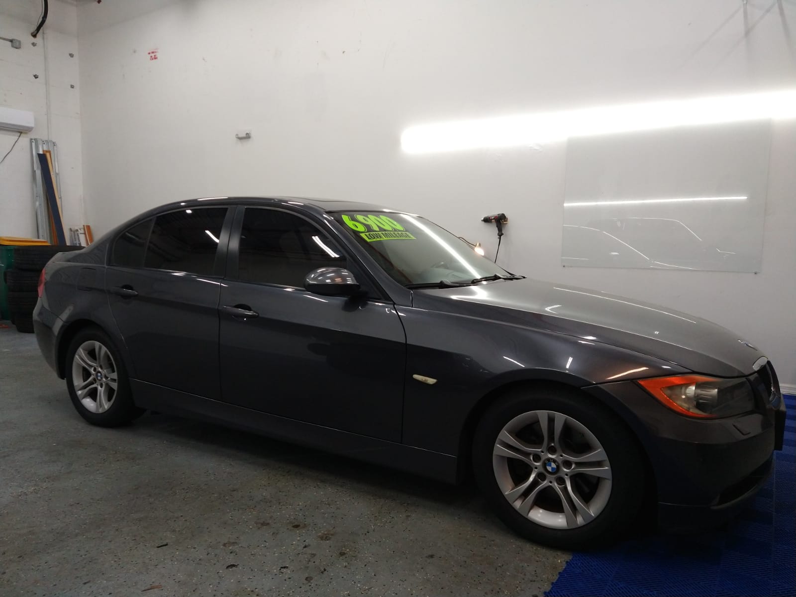 A gray car is parked in a garage with a white wall behind it
