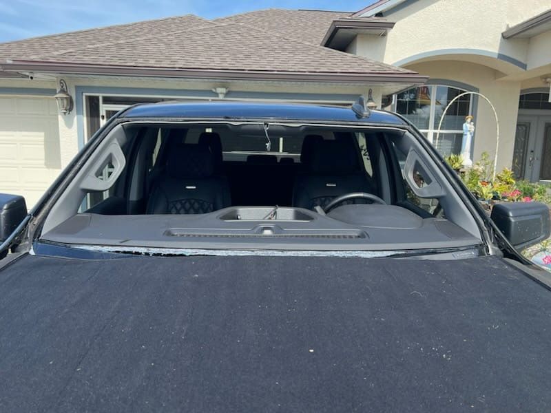 A car with a broken windshield is parked in front of a house.