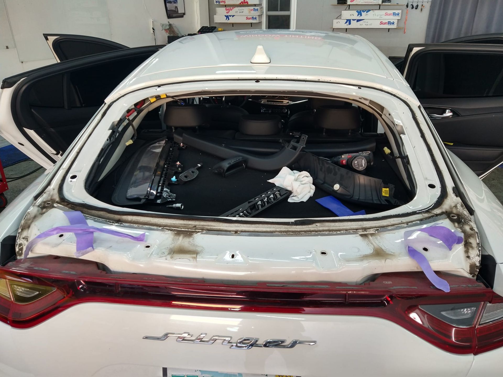 A white car with the trunk open is being worked on in a garage.