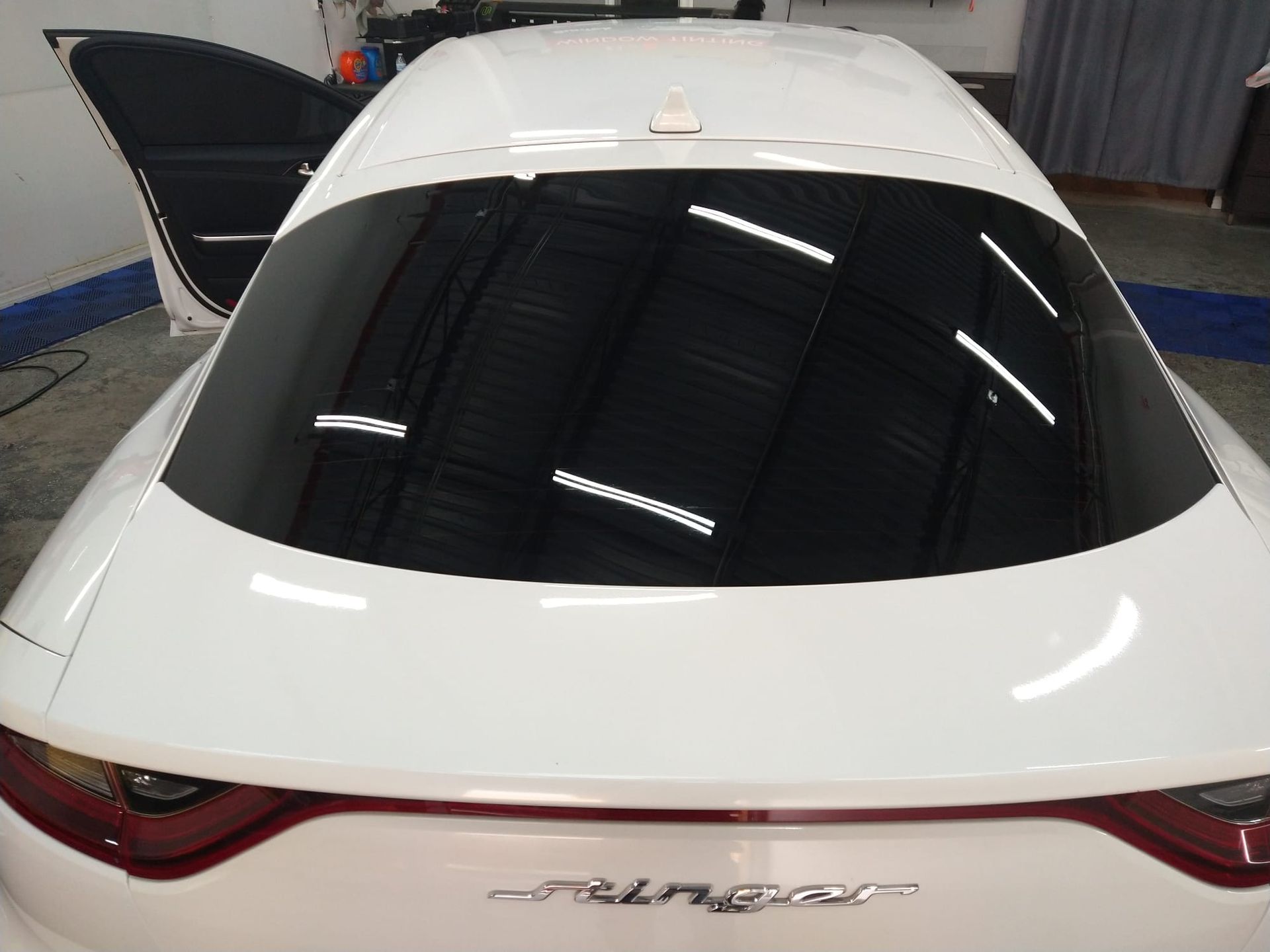 A white car with the rear window open is parked in a garage.