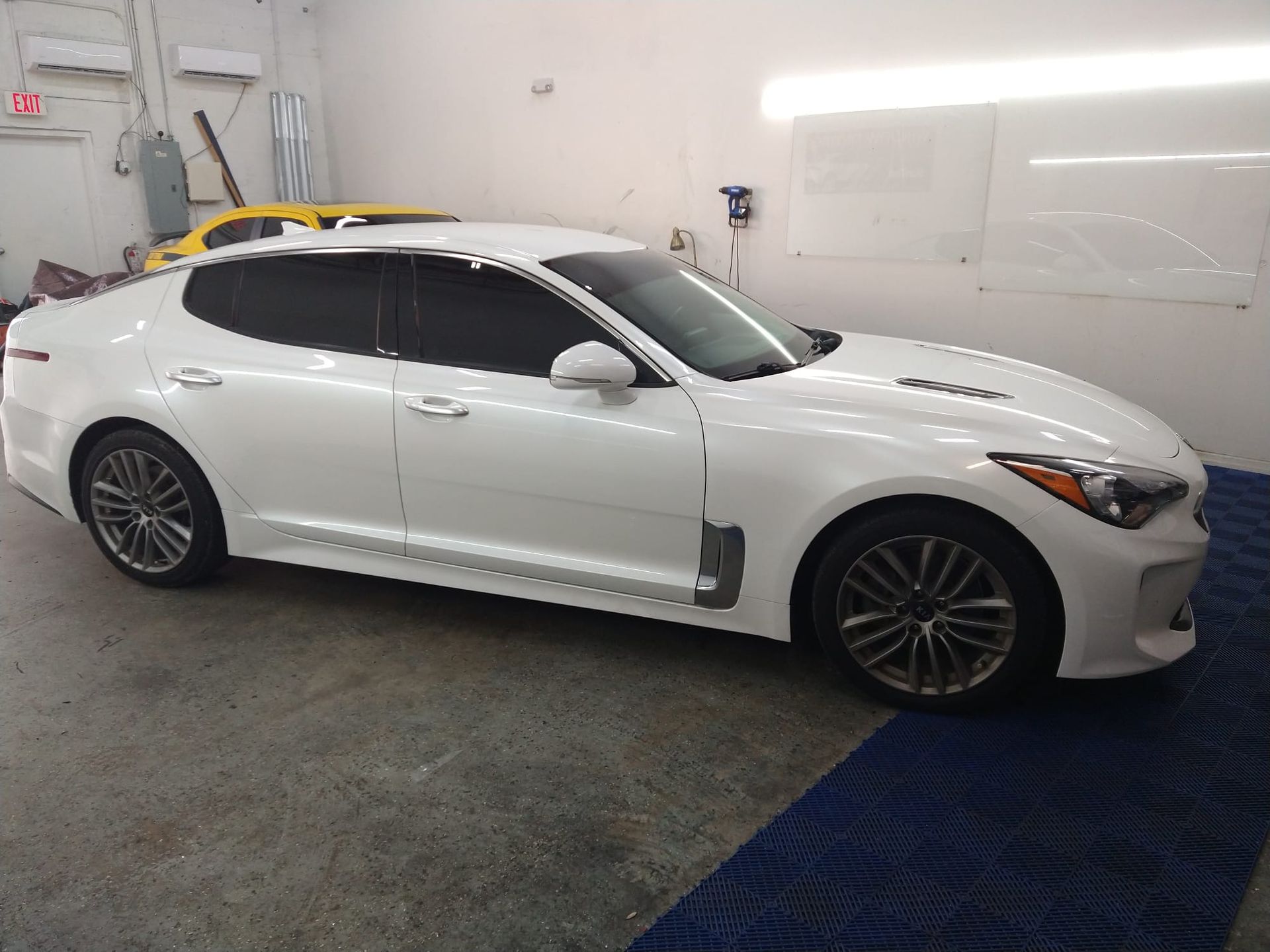 A white car is parked in a garage next to a yellow car.