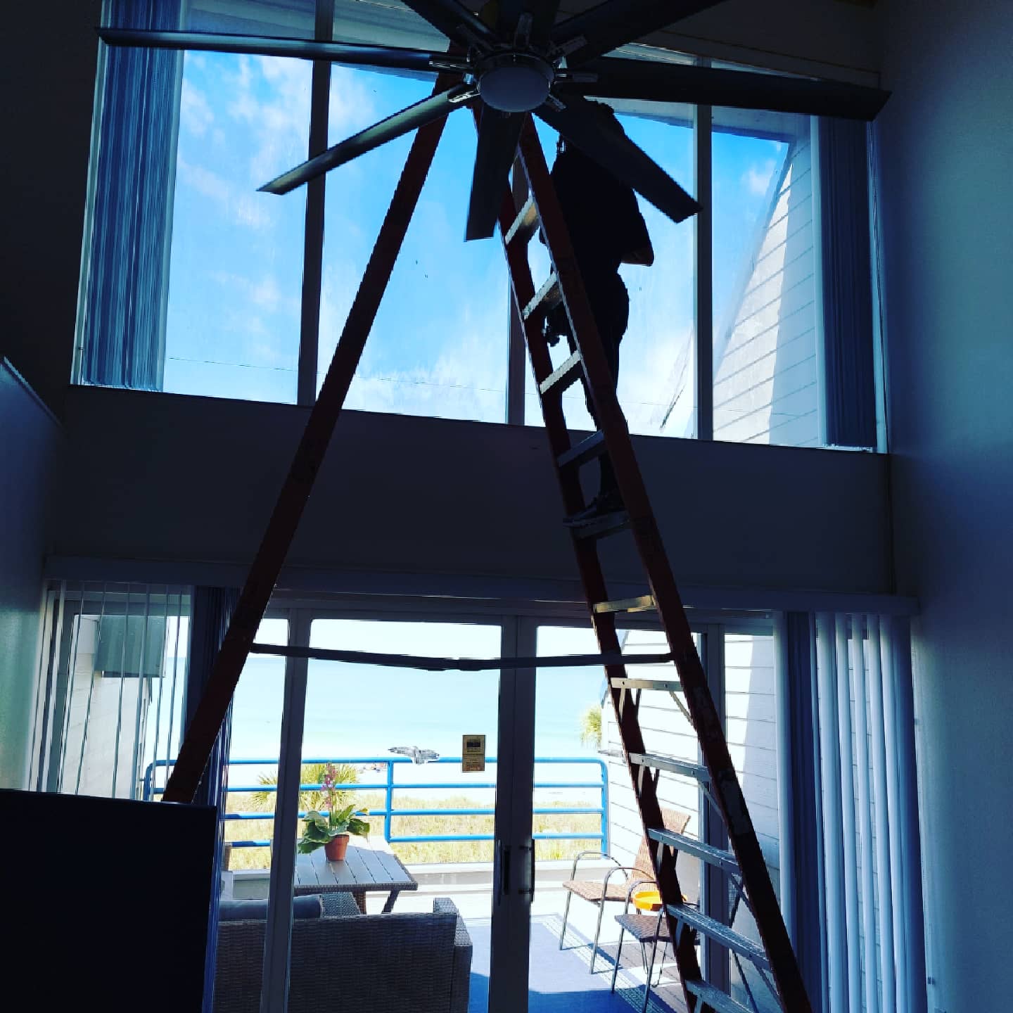 A person on a ladder looking up at a ceiling fan