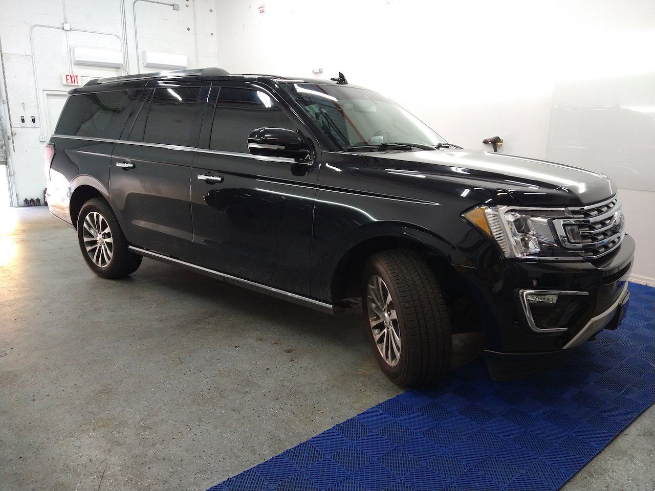 A black ford expedition is parked on a blue mat in a garage.