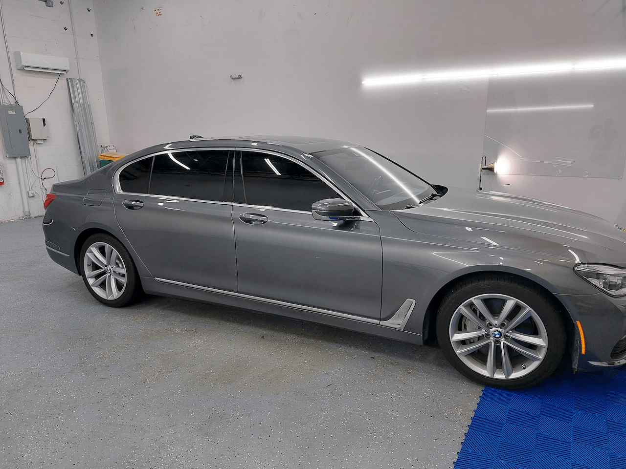 A gray car is parked in a garage next to a blue mat.