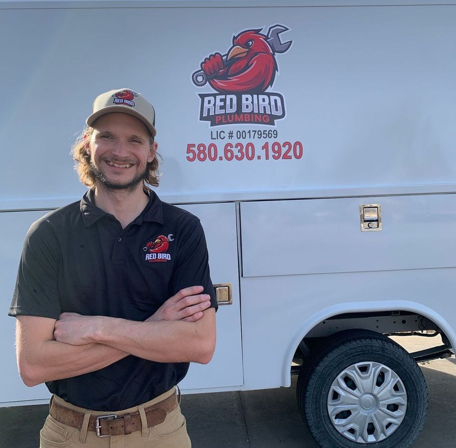 A man is standing in front of a red bird plumbing truck