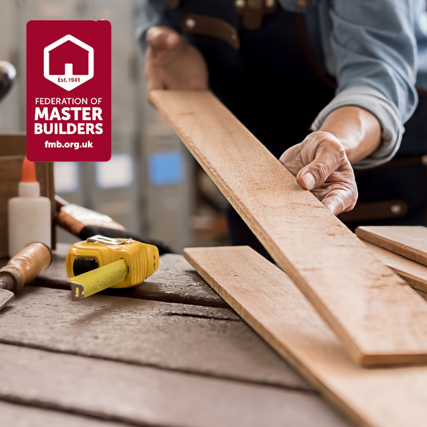 A person is measuring a piece of wood with a federation of master builders logo in the background