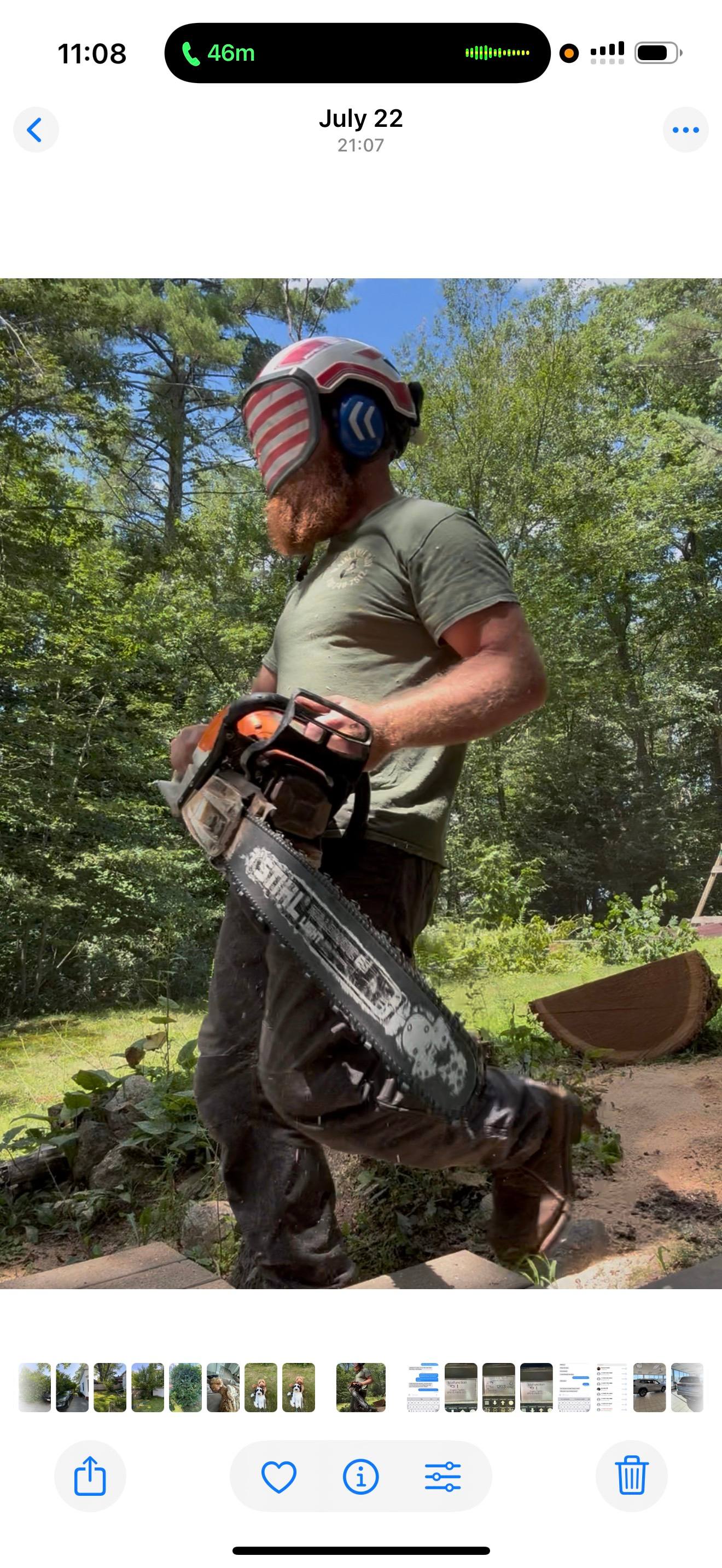 Man in safety gear holding a chainsaw in a wooded area.